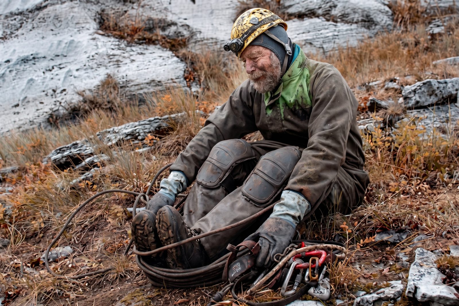 A caver sitting on the hillside after a trip, rope coiled beside him